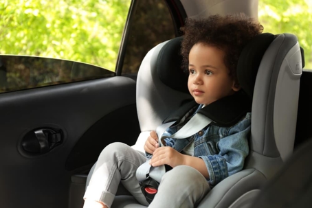 A child sits in a car seat in the back seat of a car with the window rolled down